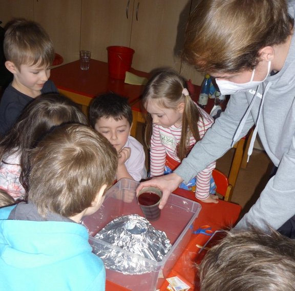 Vulkan-Experiment Ein älterer Schüler gießt etwas auf einen Vulkan aus Aluminiumpapier